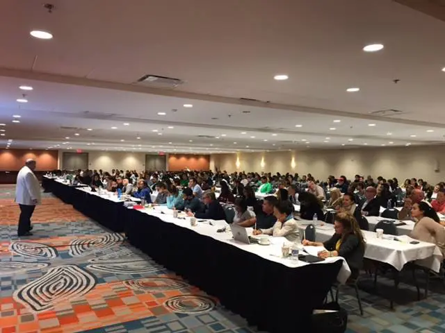 A large group of people sitting at tables in front of laptops.